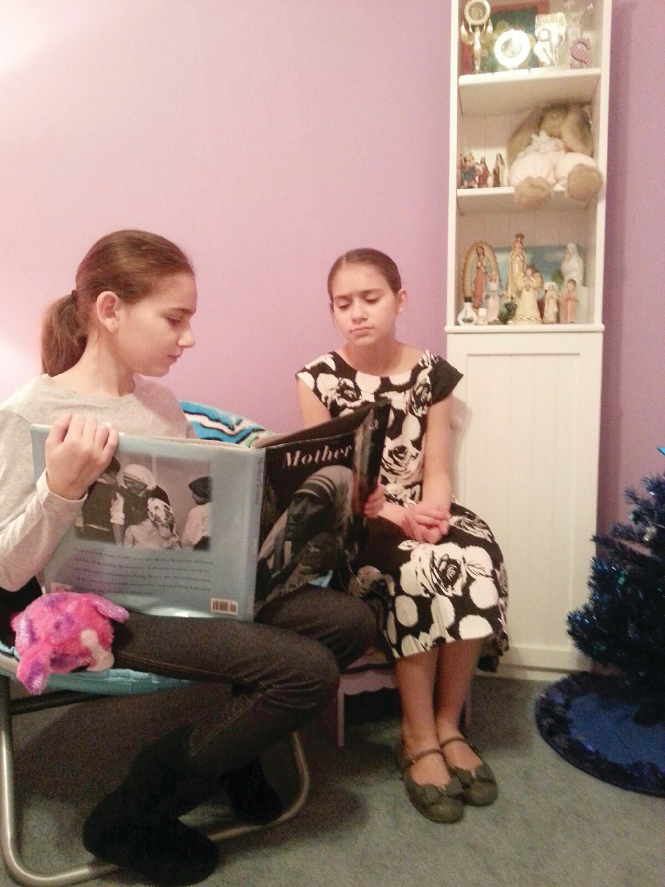 Sydney Khoury, now 13 and a seventh-grader at St. Philip School, reads one of her story books on the life of Mother Theresa with her younger sister Ava, 12, a student at St. Thomas.