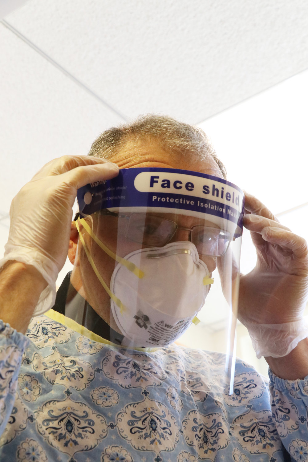 Albert Ranallo, coordinator for Pastoral Care for Health Facilities in the Diocese of Providence, adjusts his protective face shield as he suits up to minister to patients on the COVID-19 floor of the hospice facility.