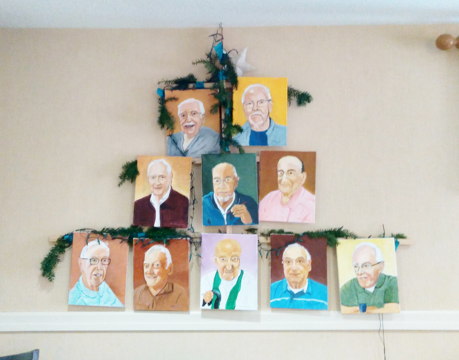 On Christmas Eve, Father Ray Tetrault gave the gift of his art to nine fellow senior priests at the St. John Vianney Residence. The artist is pictured in a self-portrait at the center of 10 paintings arranged on the wall of the residence before he presented his surprise works of art to his brother retired priests for Christmas.
