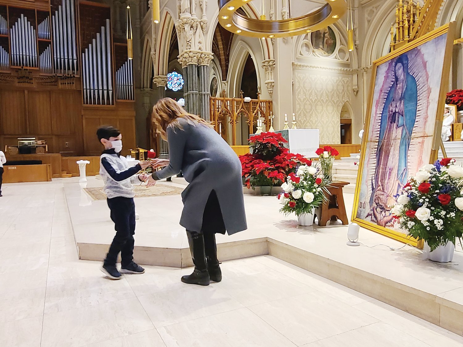 Lisa Cooley, the coordinator for the Diocese of Providence’s Office of Life & Family, helps a young parishioner from St. Charles Borromeo Church in Providence to present a rose to the pilgrimage image of Our Lady of Guadalupe during the annual Respect Life Mass at the Cathedral of Saints Peter and Paul on Jan. 23.
